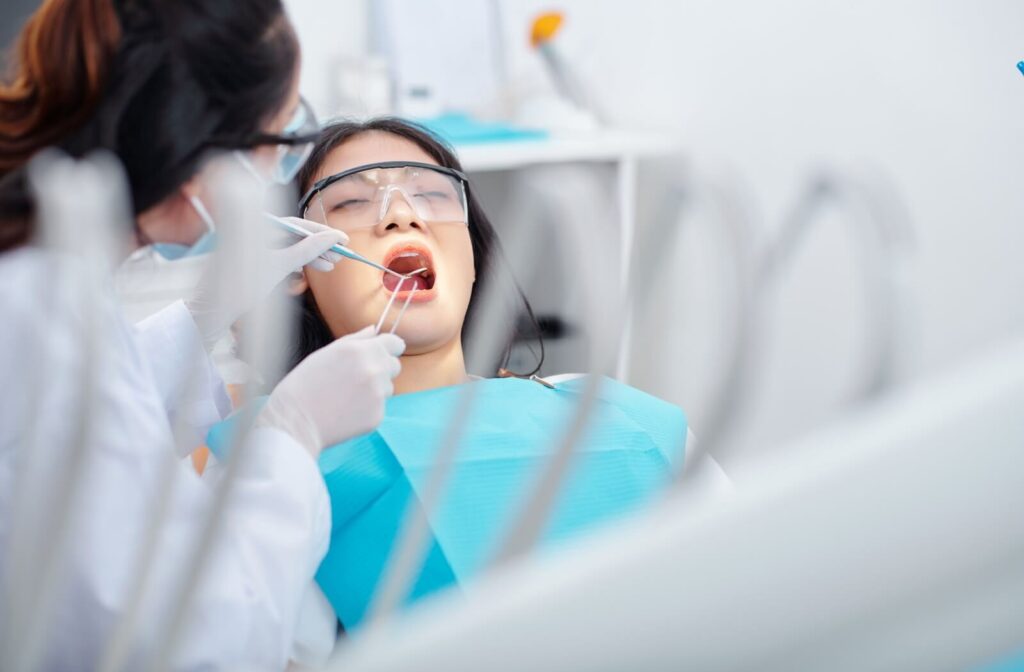 A woman undergoes a dental procedure in a clinic as a dentist inspects her mouth with dental tools.